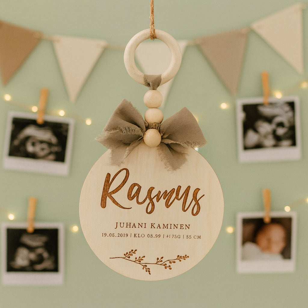 Dreamstuffin nimikyltti vauvalle – koivuvanerinen syntymätaulu beigerusetilla, ripustettuna lastenhuoneen vihreälle seinälle valokuvien ja koristevalojen joukkoon.