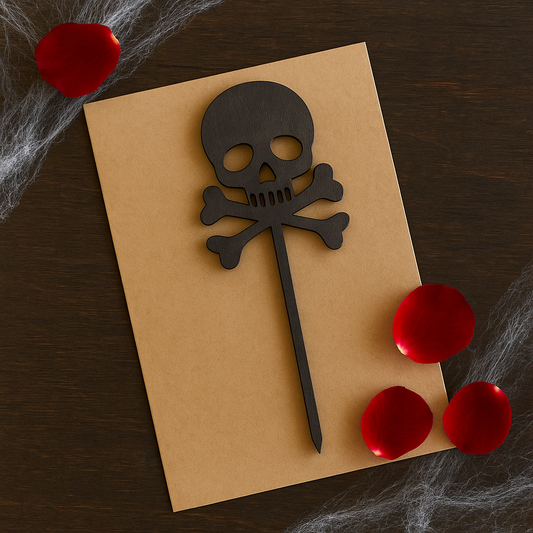 Laserleikattu pääkallo-kakkukoriste tummasta koivuvanerista, aseteltuna craft-pahville ruusun terälehtien ja hämähäkinseittien kanssa – Dreamstuff Halloween-juhlakoriste.